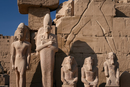 Ancient Egyptian stone statues of pharaohs standing before relief carvings at Karnak Temple Complex in Egypt