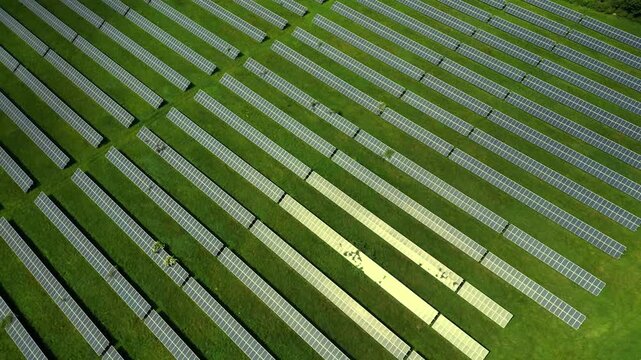 This aerial view showcases a large solar panels farm located in the UK. The layout features rows of solar panels gathering sunlight in a green field, highlighting renewable energy efforts