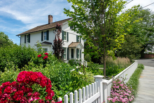 A charming white house with green shutters in a Southport (Fairfield), Connecticut neighborhood with a white picket fence and flowers.