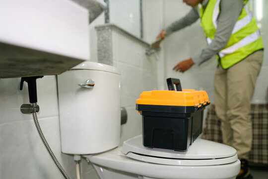 Plumber in Safety Vest Repairing Bathroom Toilet with Toolbox During House Maintenance Service