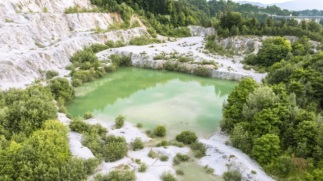 Aerial view of the turquoise pond at Kamnolom Plese pri Skofljici, surrounded by white limestone rock walls and lush green forest in Mali Vrh pri Smarju, Grosuplje, Slovenia.