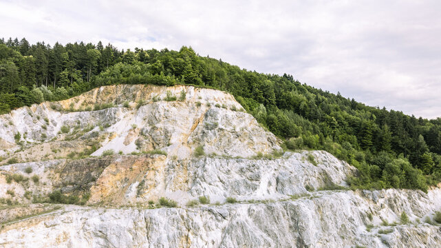 Aerial view of Kamnolom Plese pri Skofljici showing the exposed rock faces, terraced levels, and surrounding dense forest under a cloudy sky in Mali Vrh pri Smarju, Grosuplje, Slovenia.