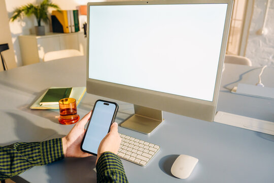 The man uses a computer and a mobile phone with a white screen