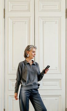 Elegant Mature Woman Using Smartphone and Holding Laptop