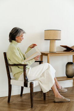 Senior Woman Reading Book in Modern Minimalist Interior