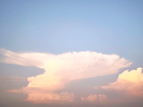 Towering cumulonimbus clouds illuminated by sunset hues beneath expansive blue sky.