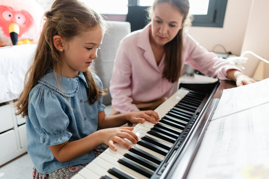 Young girl learning piano keyboard with music teacher