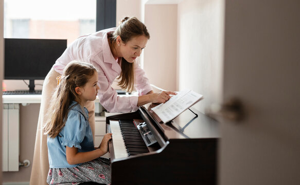 Woman teaching young girl playing piano music