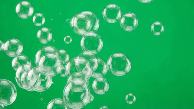 Transparent soap bubbles floating and rising against a vibrant green background abstract motion playful celebration lightheartedness and joy
