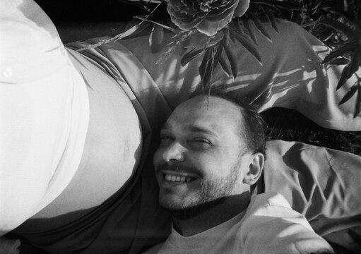 A man lies next to a pregnant belly and smiles at the camera.