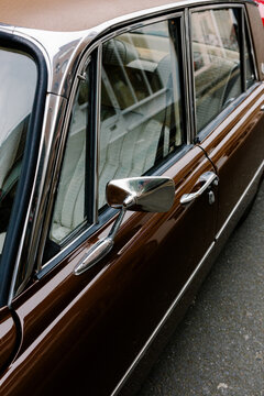 Side view of a classic brown car with chrome trim on a paved street.