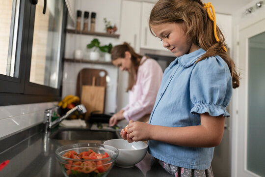 Daughter learning cooking skills helping mother in kitchen