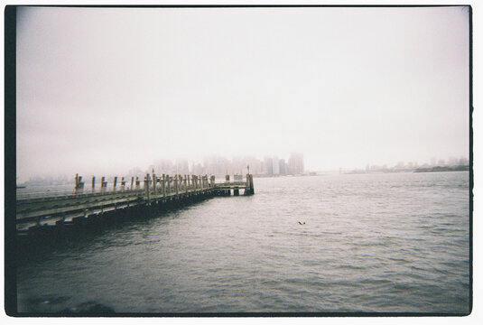 Wooden pier extending into East River with Manhattan skyline in fog