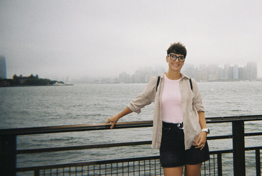 Woman smiling by water, New York City skyline in mist