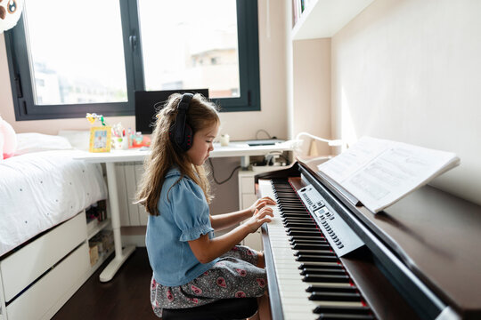 Girl learning piano at home wearing headphones
