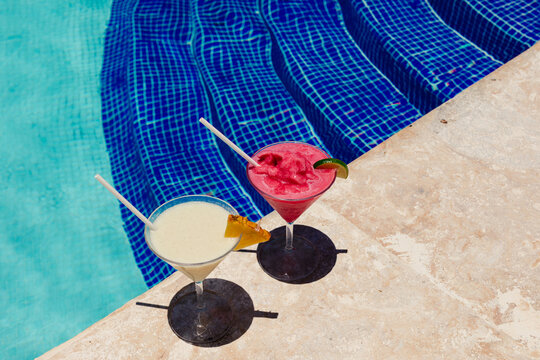 Two frozen cocktails on a pool edge with sharp shadows on stone