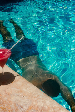 Swimmer in a turquoise pool with a red cocktail on the deck.