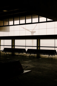 Empty airport hall with seats facing a wind turbine in the fog
