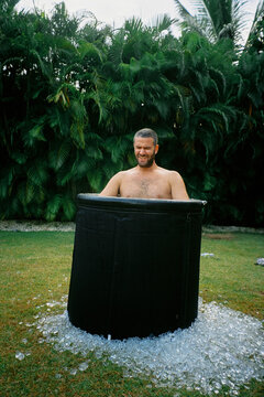 Man taking an ice bath in a plastic tub in a garden