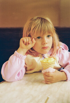 Child Sits at Table With Ice Cream on a Sunny Day