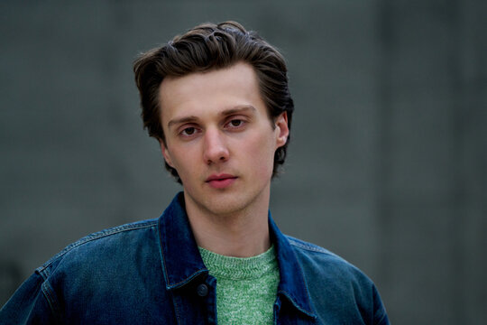 Young Man Poses in Denim Jacket Against Gray Background