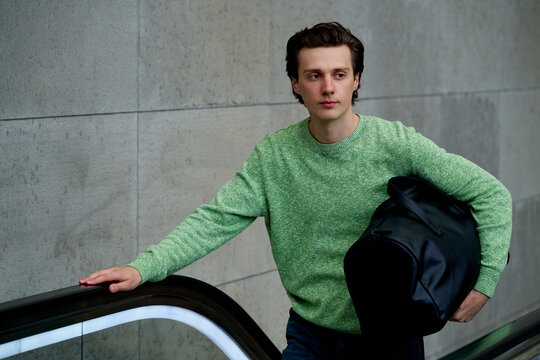 Young Man Rides Escalator While Holding Bag in a Building