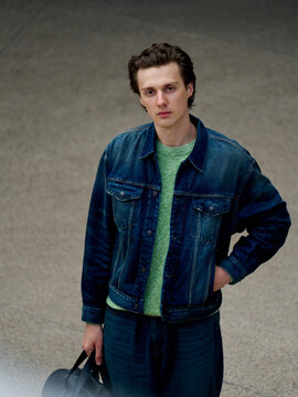 Young Man in Denim Jacket Stands Still in Urban Area