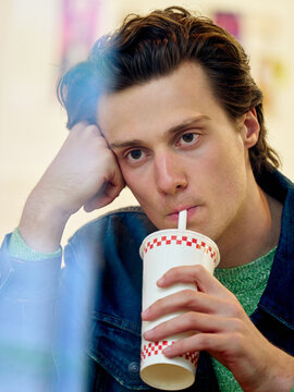 Young Man Drinks From a Cup While Sitting Indoors at a Fast Food Place