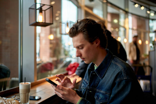 Young Man Uses Smartphone While Sitting in Cafe