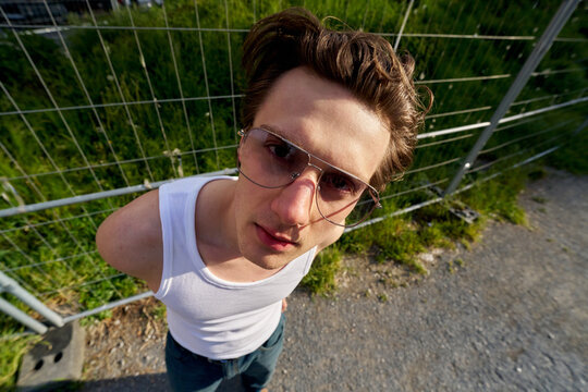 Young Man Wearing Sunglasses Stands Near a Fence in Daylight