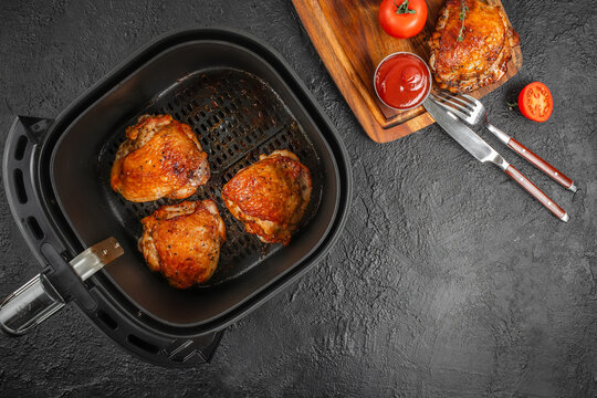 Air fryer chicken thighs with ketchup sauce and cutlery on black background top view