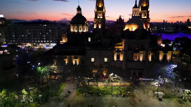 Drone elevating video of Tapatia Plaza, Guadalajara at night. Illuminated fountain and vibrant city life at dusk.