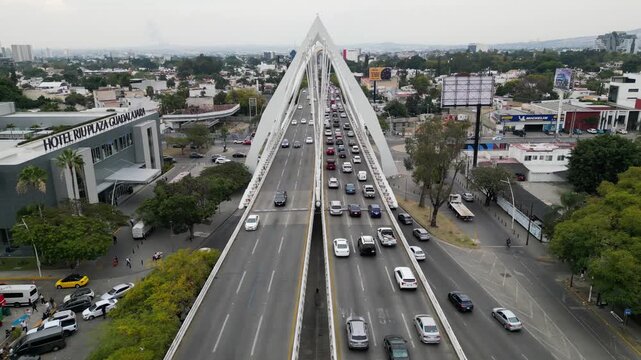 Guadalajara, Mexico - February 6 2026: Aerial footage showcases the modern Matute Remus Bridge in Guadalajara, bustling with urban city traffic and a vibrant cityscape. A high angle view of the iconic