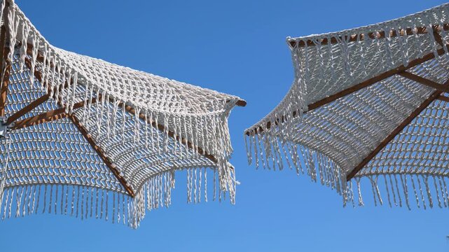 Close-up of stylish bohemian sunshades with long cotton fringes under a bright sunny sky, concept of peace, luxury relaxation, and seaside vacation
