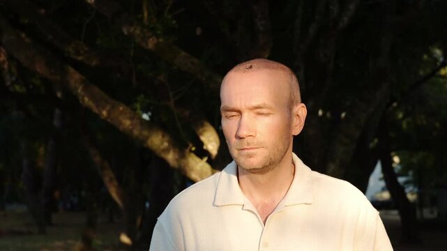 A portrait of a middle-aged man after a hair transplant procedure, looking disappointed and shaking his head with a skeptical expression, standing outdoors against trees in Portugal