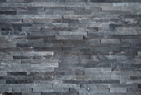 Background of textured natural stone tiles in grey color, modern dark gray slate stone wall cladding texture, elegant grey quartzite brick wall background for contemporary design