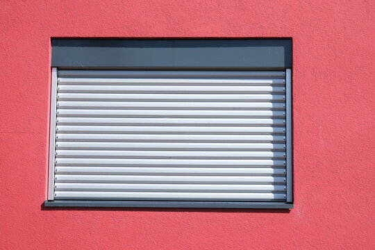Rote Hauswand mit Fenster und heruntergelassenem Rollladen bei starker Hitze im Hochsommer