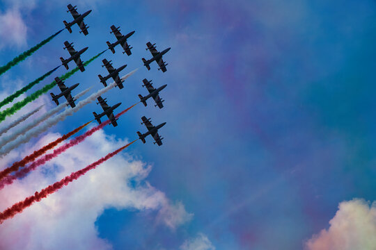 Italy , Aerobatic jet team performing precision formation flight. High-speed military aircraft trailing colored smoke during airshow demonstration.