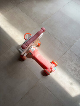 Children&rsquo;s scooter resting on a polished granite tile floor as natural sunlight streams indoors, creating striking light and shadow patterns that enhance the playful and minimalist composition.