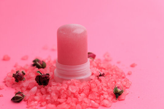 Natural crystal alum deodorant displayed on pink salt with dried rose buds in a simple setup