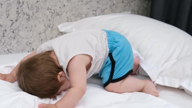 Playful baby boy headbanging or hiding face on white bed sheets