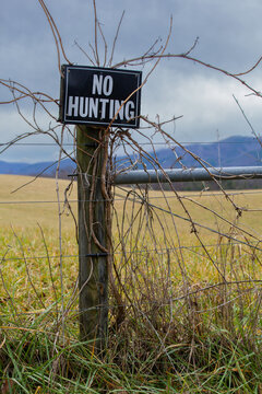 No Hunting Sign on Fence in Rural Field Landscape with Farmland and Open
