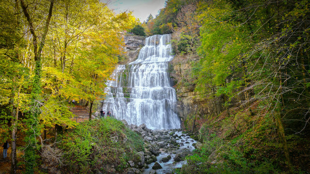 Aerial view of Cascades du Herisson waterfall surrounded by vibrant autumn foliage and lush forest in Le Frasnois, Bourgogne-Franche-Comte, France.