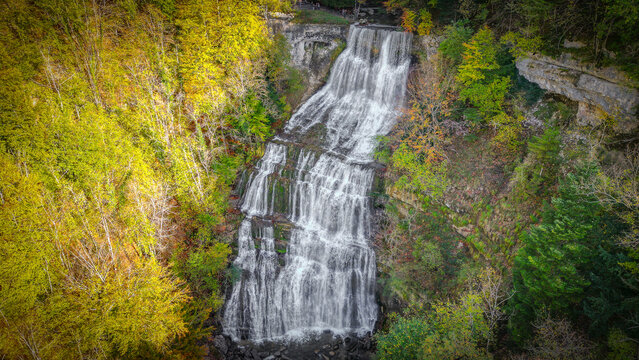 Aerial view of Cascades du Herisson surrounded by vibrant autumn foliage and rocky cliffs in Le Frasnois, Bourgogne-Franche-Comte, France.