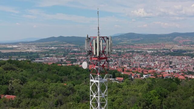 View of a cell tower overlooking a city with hills and fields in the background
