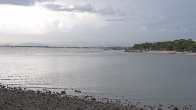 calm waters and a tree lined shoreline along north pattaya coastline in thailand beneath dramatic monsoon clouds and soft evening light