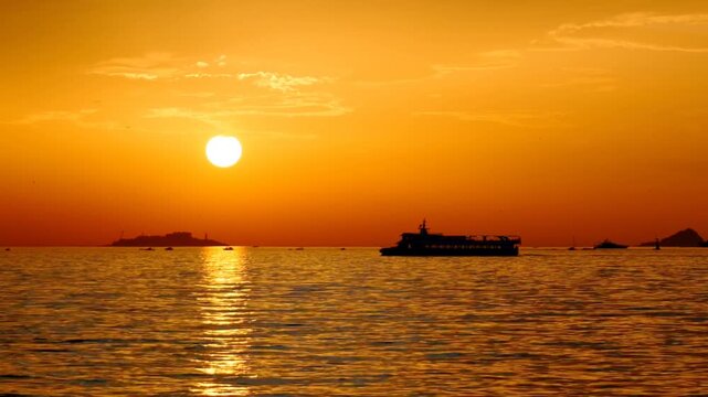 Passenger ferry sailing towards a bright golden sunset on the Sea of Marmara, with the distinct silhouette of Yassiada visible in the background in Istanbul, Turkey. Zoom-out shot