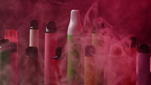 Colorful disposable electronic cigarettes in thick vape smoke on red background.