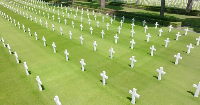 High angle view showing endless rows of symmetrical white marble crosses standing perfectly aligned on a pristine green lawn at a historic military cemetery. Many cypress trees line the tombs.