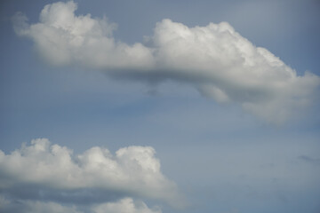 Fluffy white cumulus clouds drifting across a clear blue sky © Thanakrit